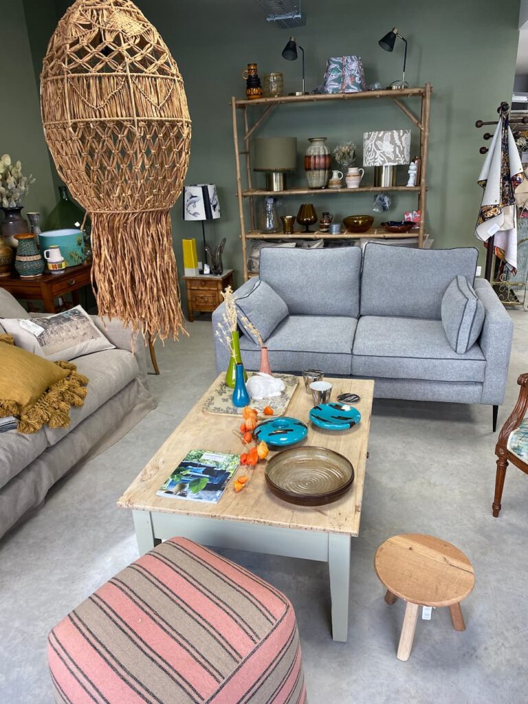 Coin salon de la boutique avec canapé gris, pouf rayé et objets déco, atelier tapissier à Albi